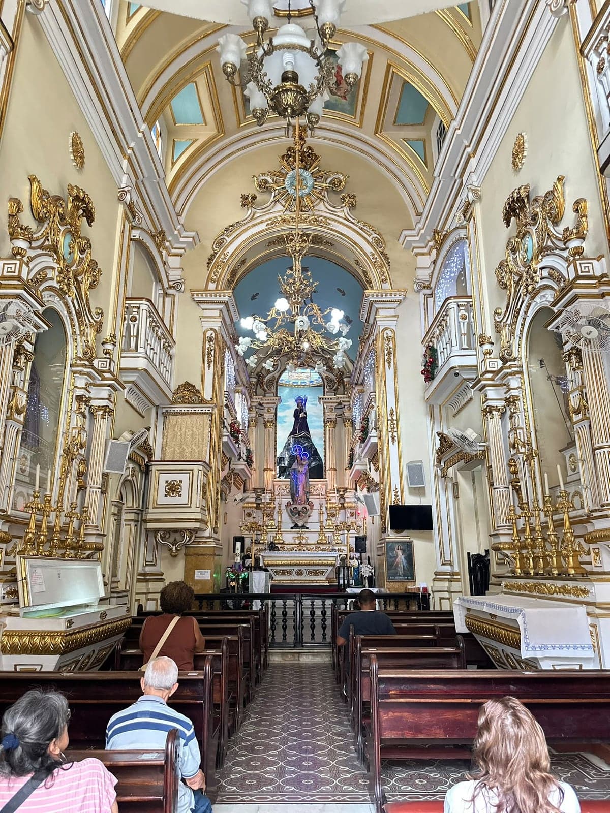 Interior de uma igreja, com detalhes arquitetônicos e ornamentação dourada.